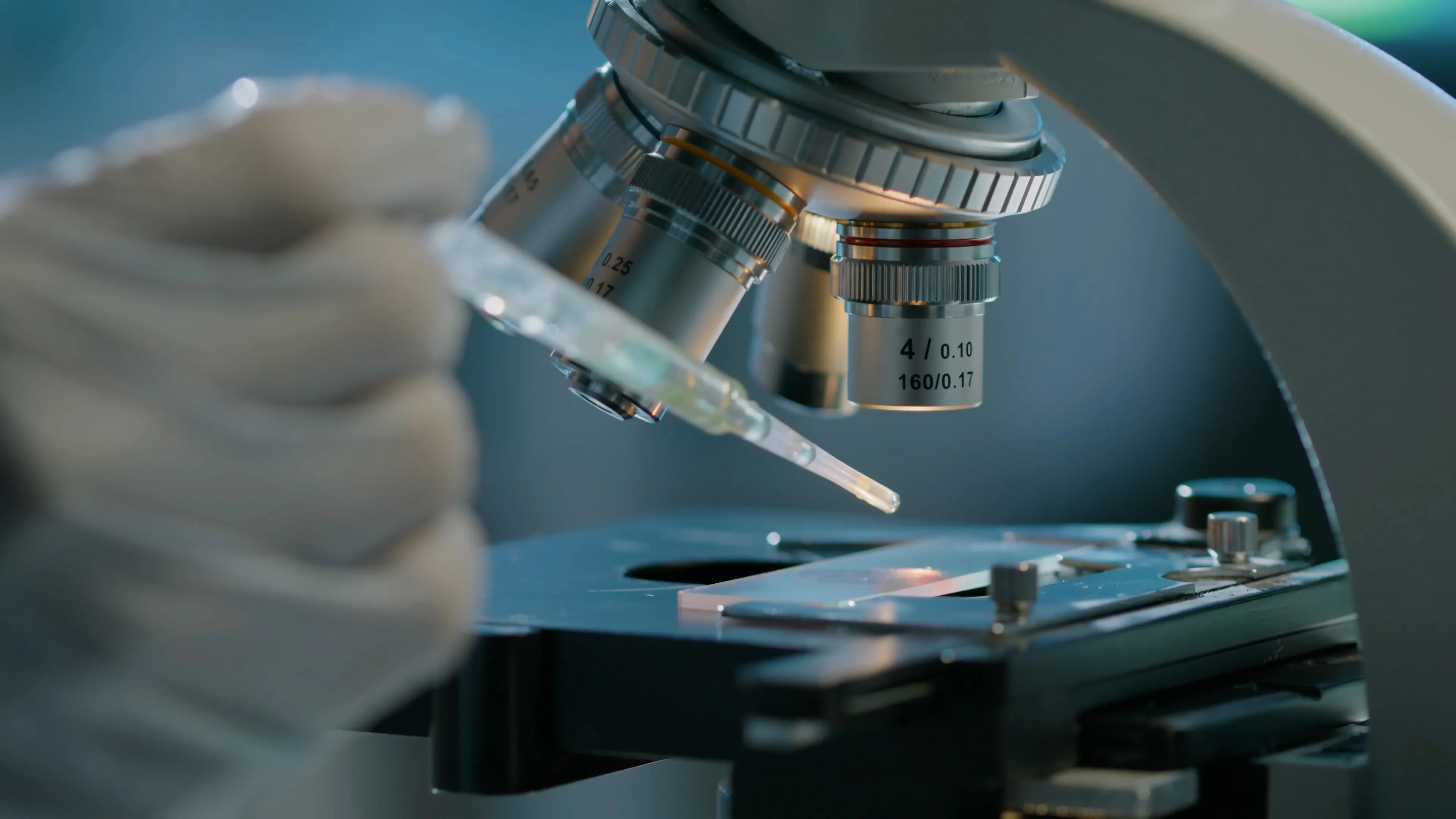 Gloved hand loading a specimen slide into a microscope